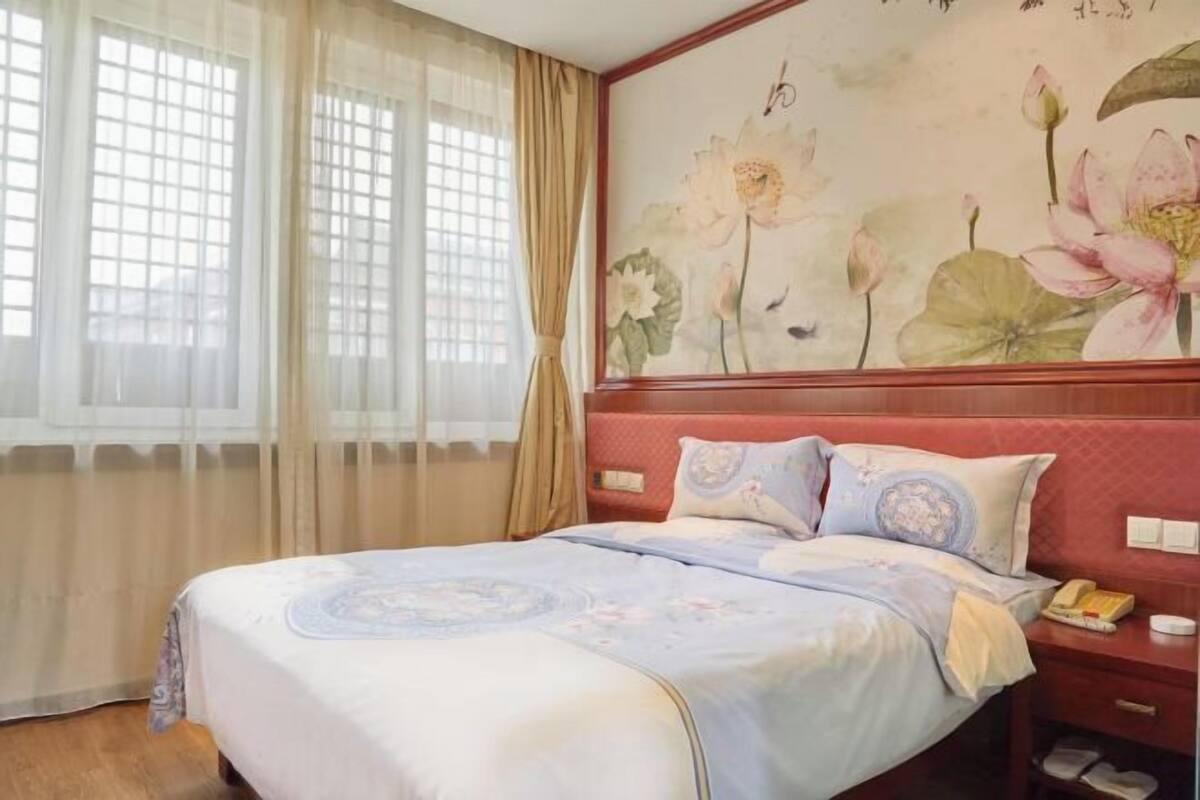 Una habitación de hotel con una cama, una mesita de noche, un teléfono y una ventana con cortinas translúcidas.