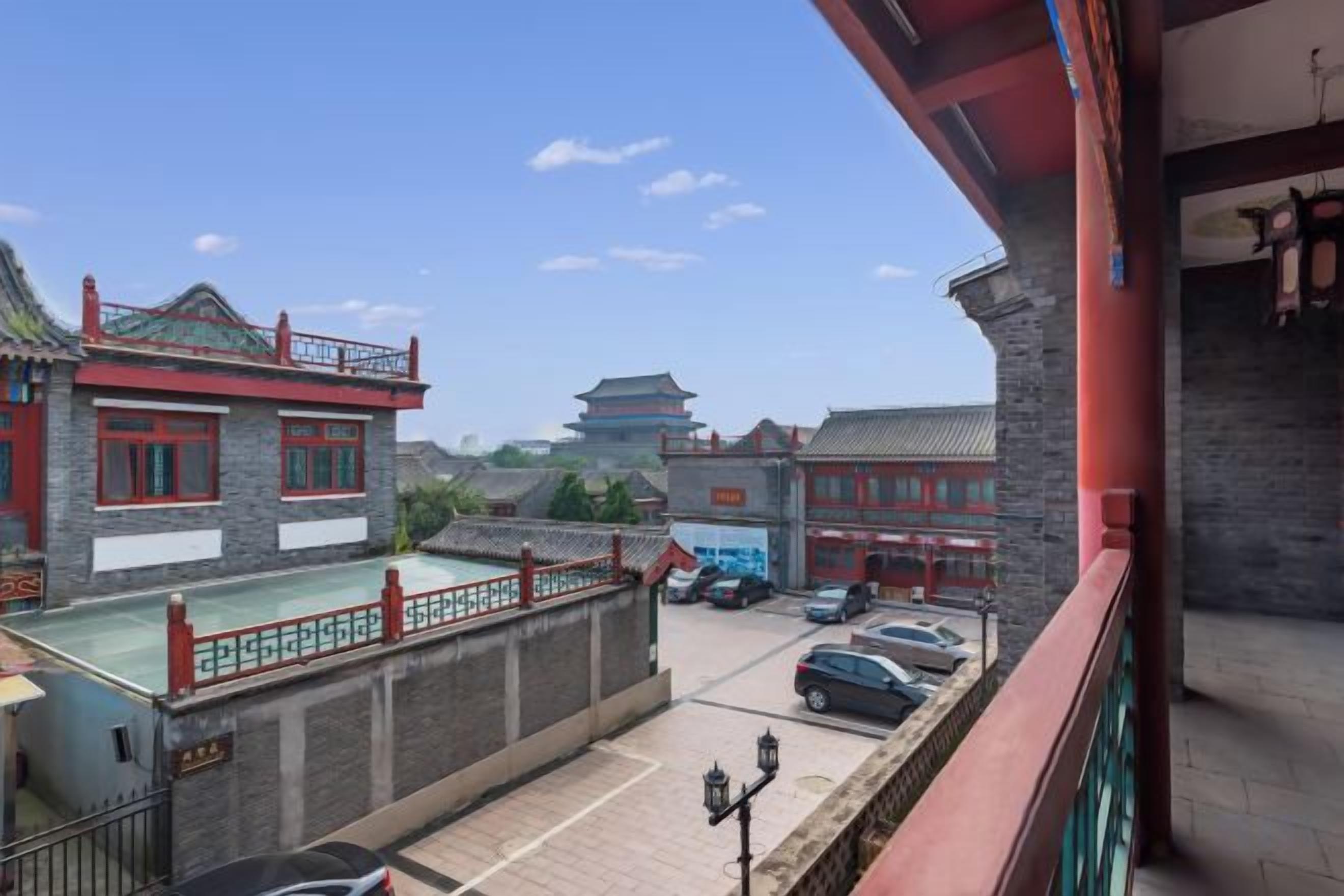 A traditional building with a red roof and white walls, a parking area with cars, and a clear sky.