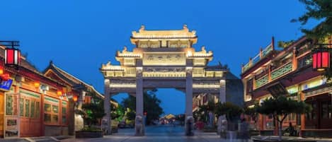 Une porte chinoise traditionnelle aux motifs complexes, un chemin pavé et des bâtiments de chaque côté.