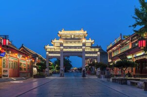 A traditional Chinese gate with intricate designs, a paved walkway, and buildings on either side.