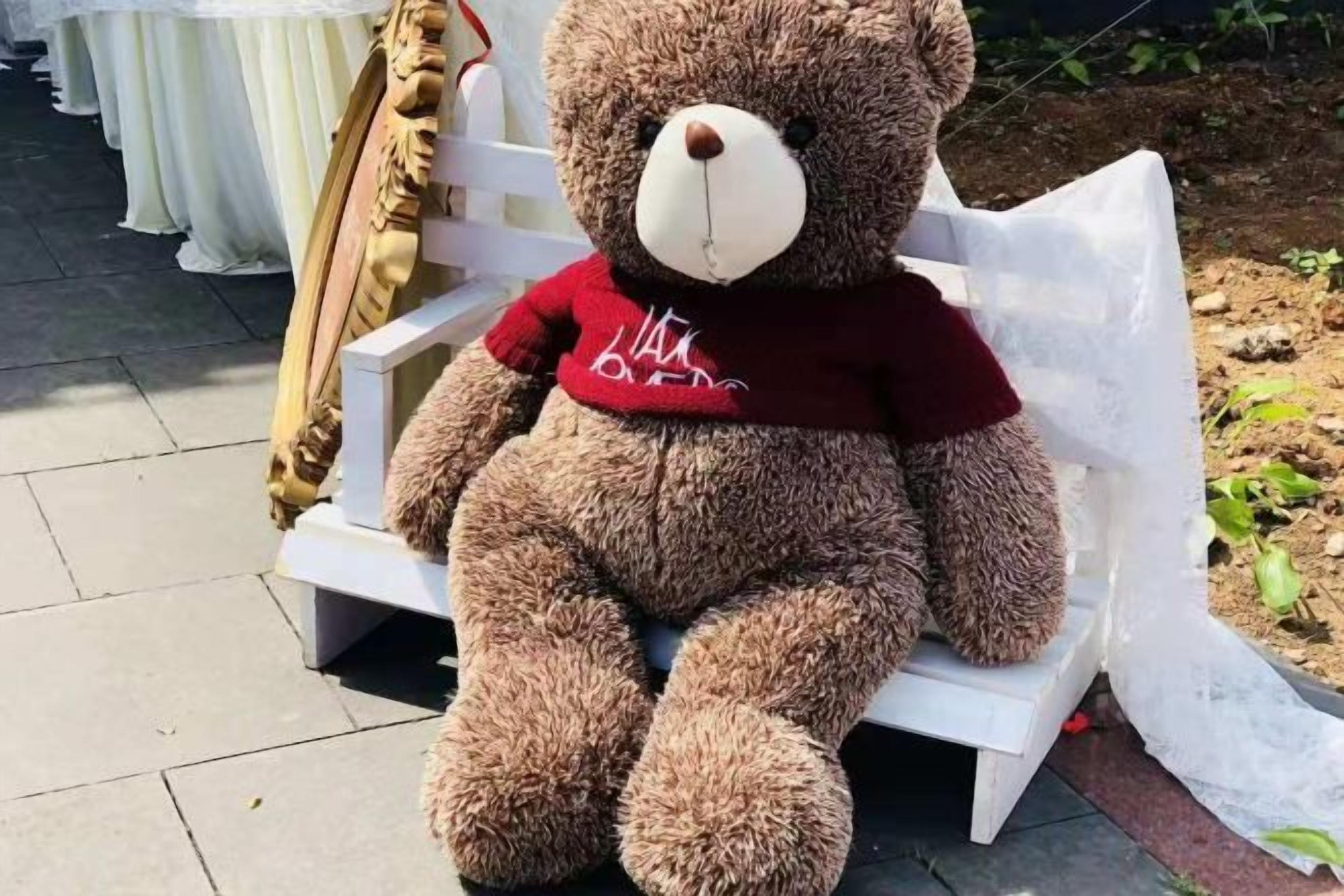Un oso de peluche grande sentado en un banco blanco.