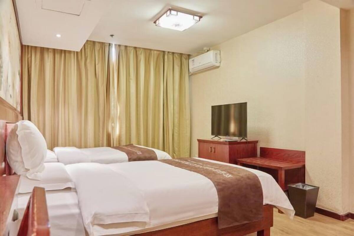 Habitación de hotel con dos camas, un televisor sobre un mueble de madera y un aire acondicionado en la pared.