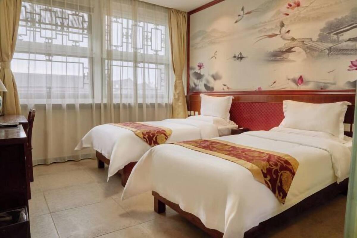 Habitación de hotel con dos camas, un escritorio y una ventana con cortinas traslúcidas.
