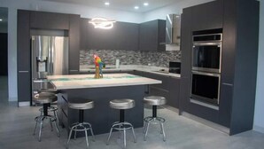 Une cuisine moderne dotée d’un îlot central, de tabourets de bar et d’appareils électroménagers intégrés.