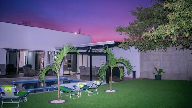Un espace piscine extérieur moderne, doté de chaises longues et de palmiers.