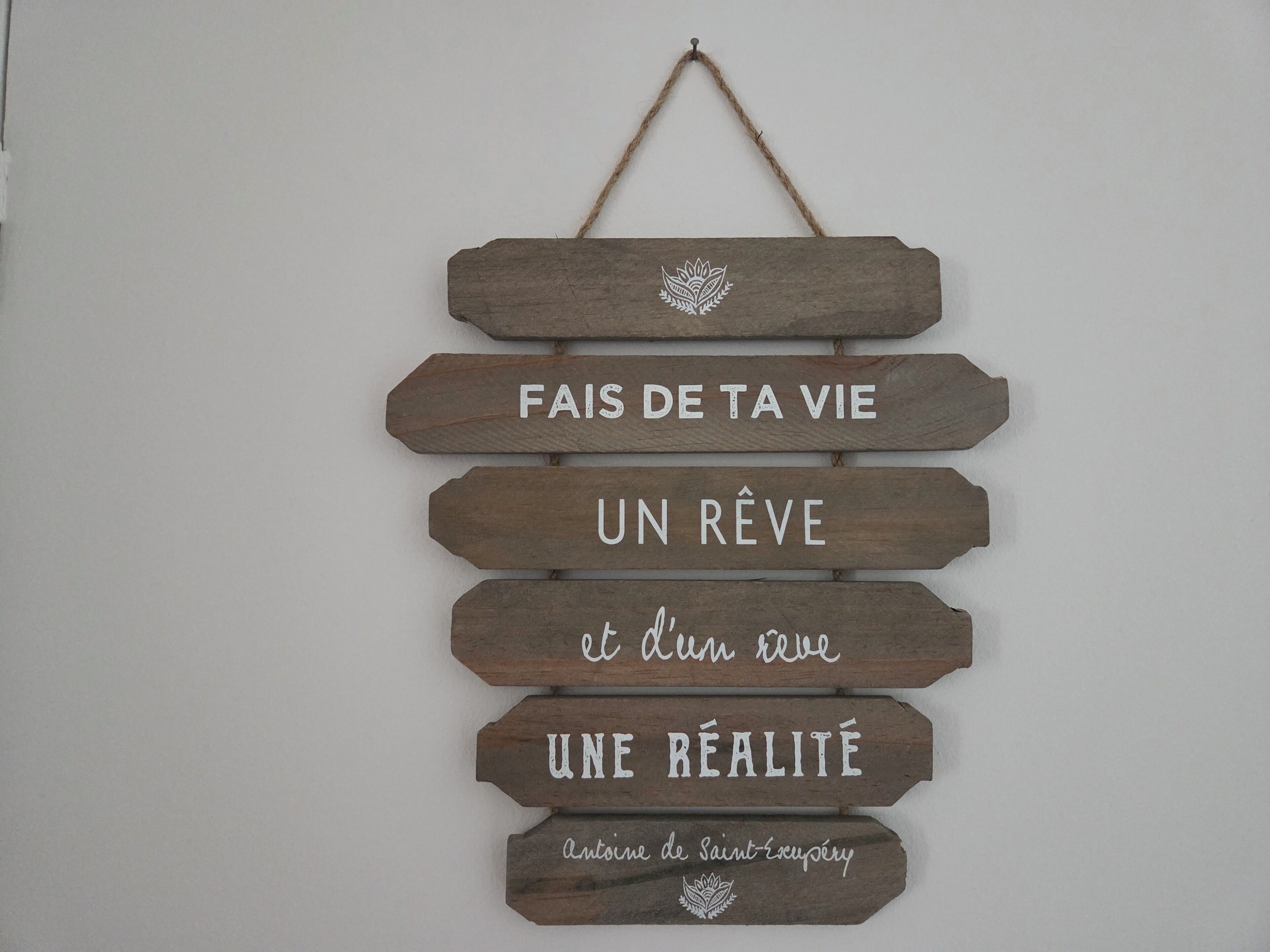 Ein hölzernes Schild mit der Aufschrift 'Fais de ta vie un rêve et du rêve une réalité' und 'Antoine de Saint-Exupéry'.