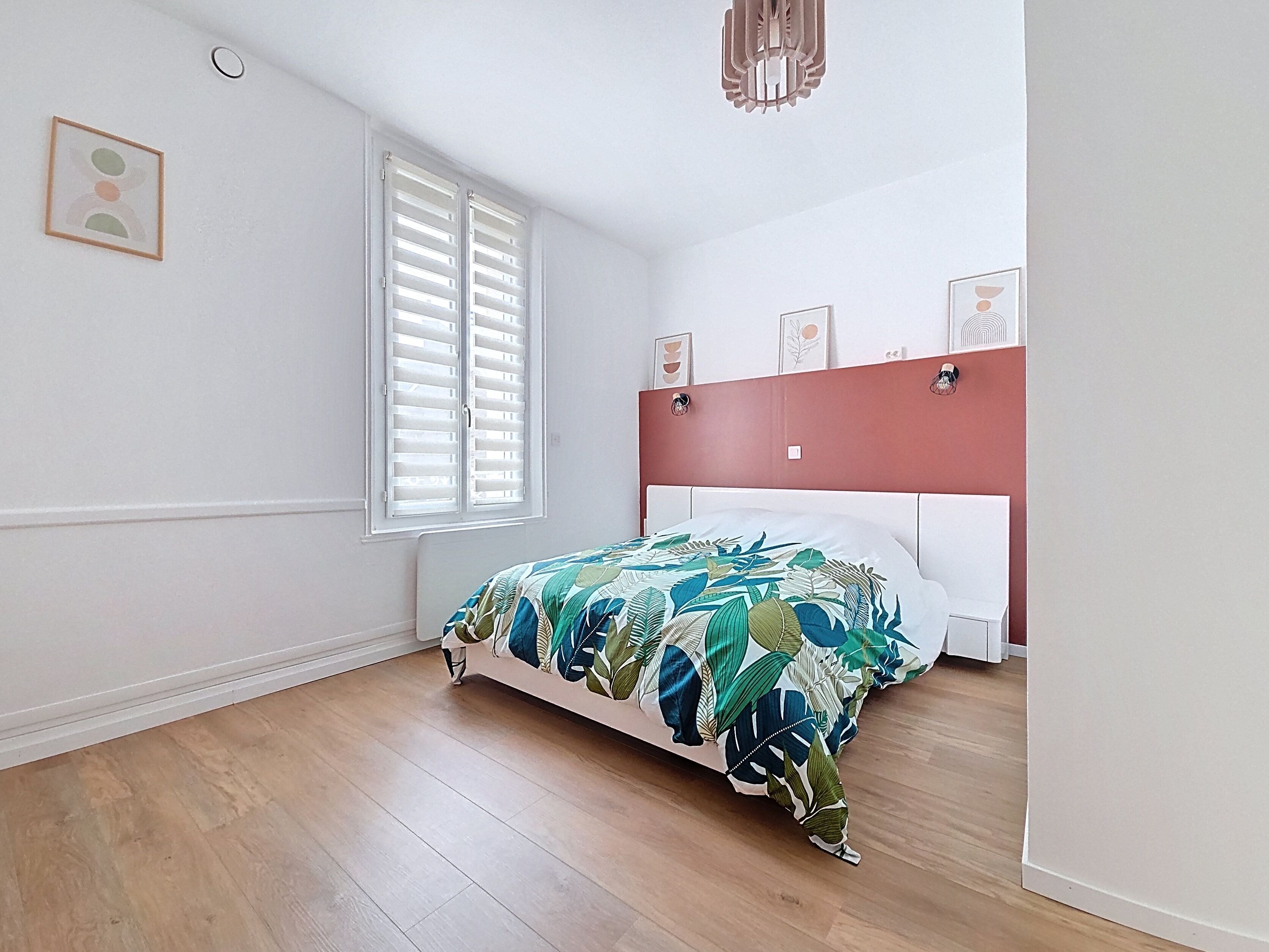 Un dormitorio con cama, ventana con persianas, pared de acento roja y lámpara en el techo.