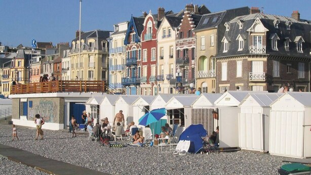 Een strandboulevard met kleurrijke gebouwen, buitenzitplaatsen en een rij strandhutten.