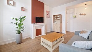 Een woonkamer met een tv op een schoorsteenmantel, een bank, een salontafel en een kastje met een 'HOME' bord.