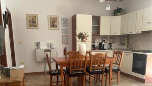 A dining area with a wooden table and chairs, a kitchen with white cabinets, and a herringbone-patterned floor. - Magic Living Home Apartment on the crystal clear sea of Calabria (Campora San Giovanni)