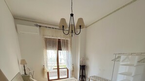 A bedroom with a bed, a bedside table, a lamp, a window with curtains, a chandelier, and a wardrobe. - Magic Living Home Apartment on the crystal clear sea of Calabria (Campora San Giovanni)