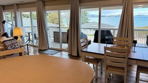 A room with a large window, a dining table, chairs, a lamp, and a view of the outdoors. - Mission Mountain Shores at Flathead Lake (Polson)