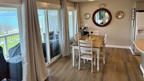 A dining area with a wooden table and chairs, a large mirror on the wall, and a view of a lake through the windows. - Mission Mountain Shores at Flathead Lake (Polson)