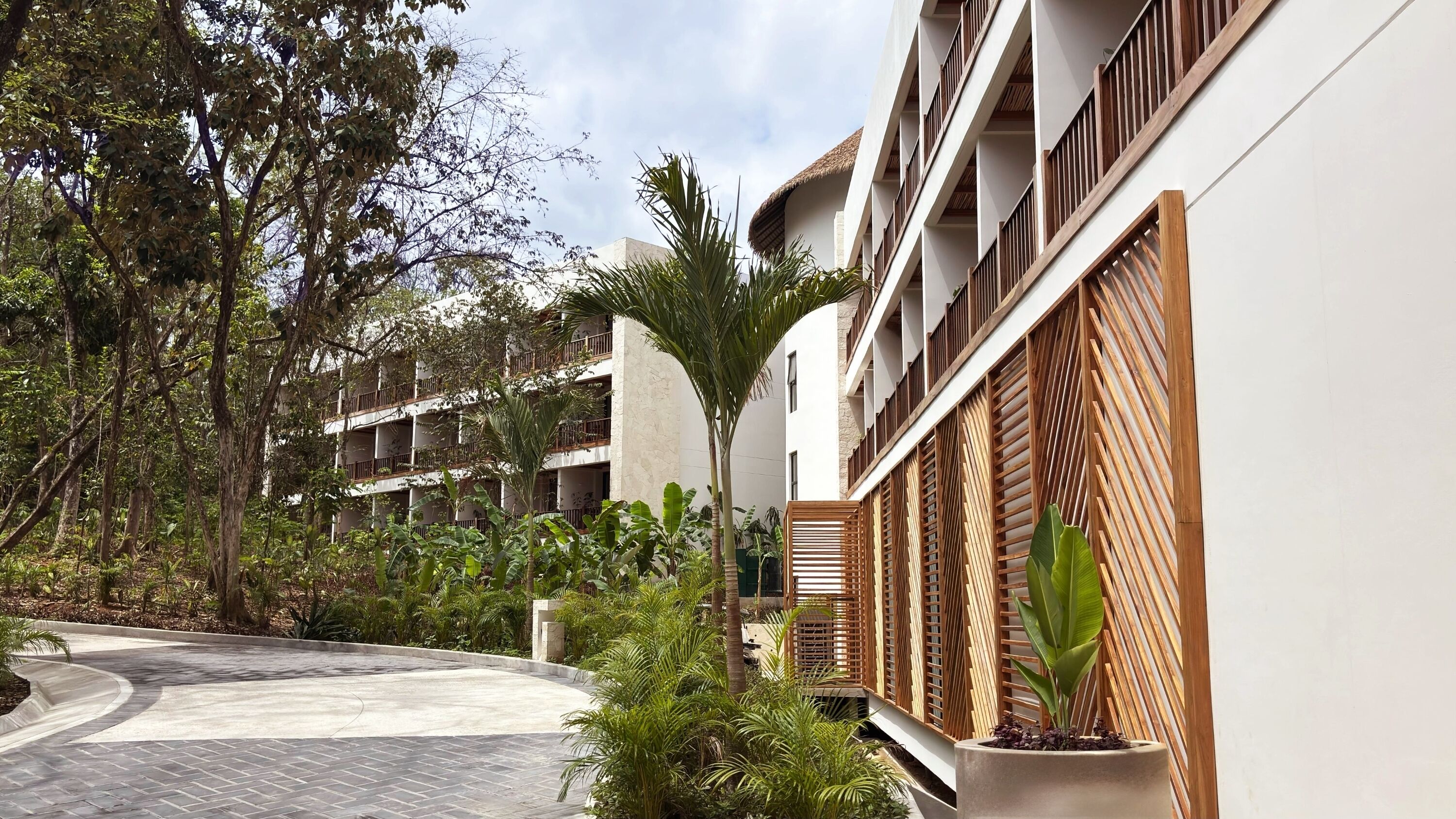 A courtyard with a curved pathway, surrounded by lush greenery and a multi-story building with balconies.