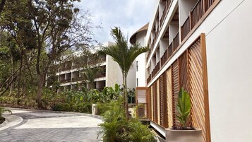 Un patio con un sendero curvo, rodeado de abundante vegetación y un edificio de varios pisos con balcones.