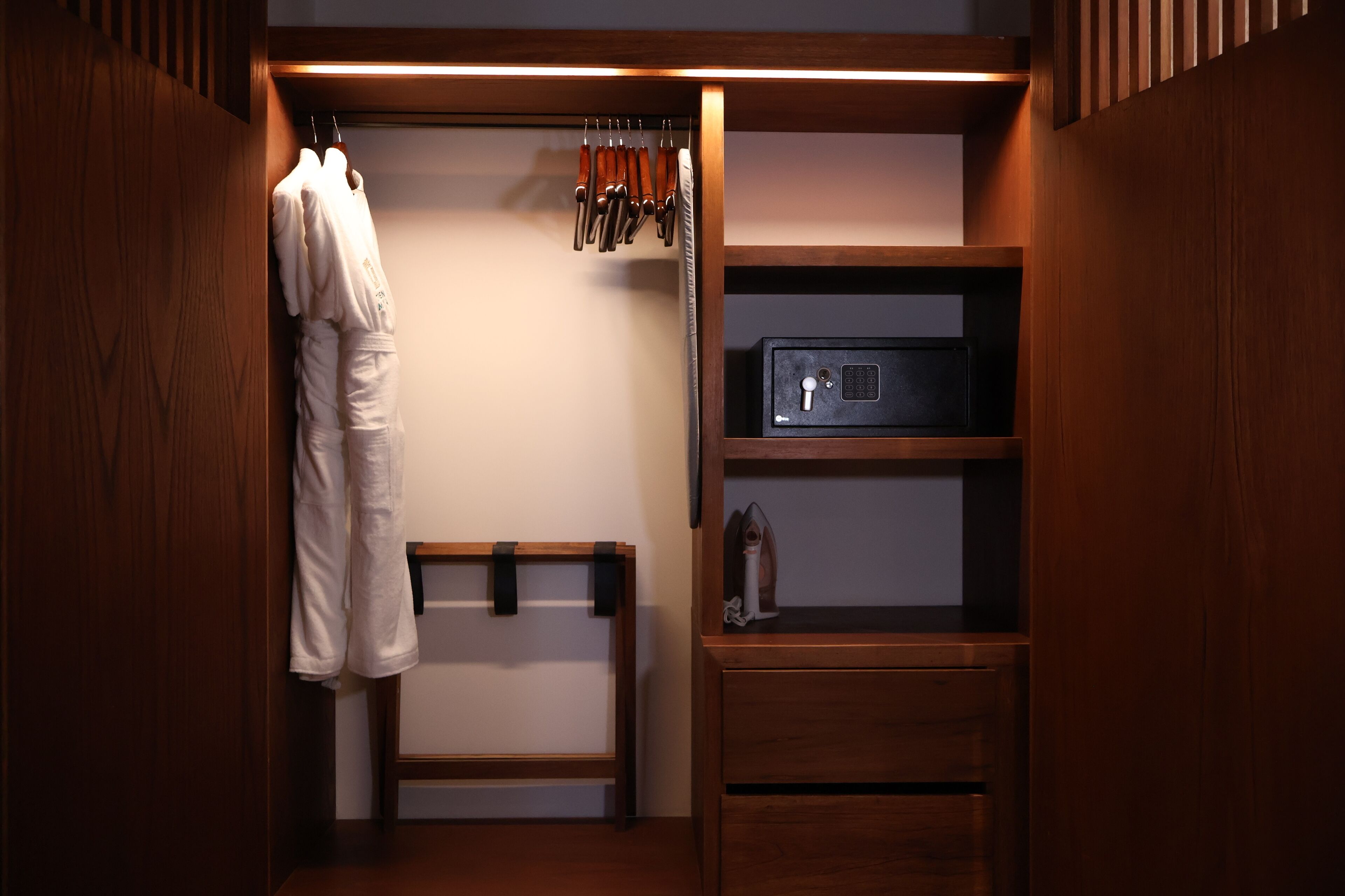 A wooden closet with a hanging rack, a shelf with a safe, and a bench.