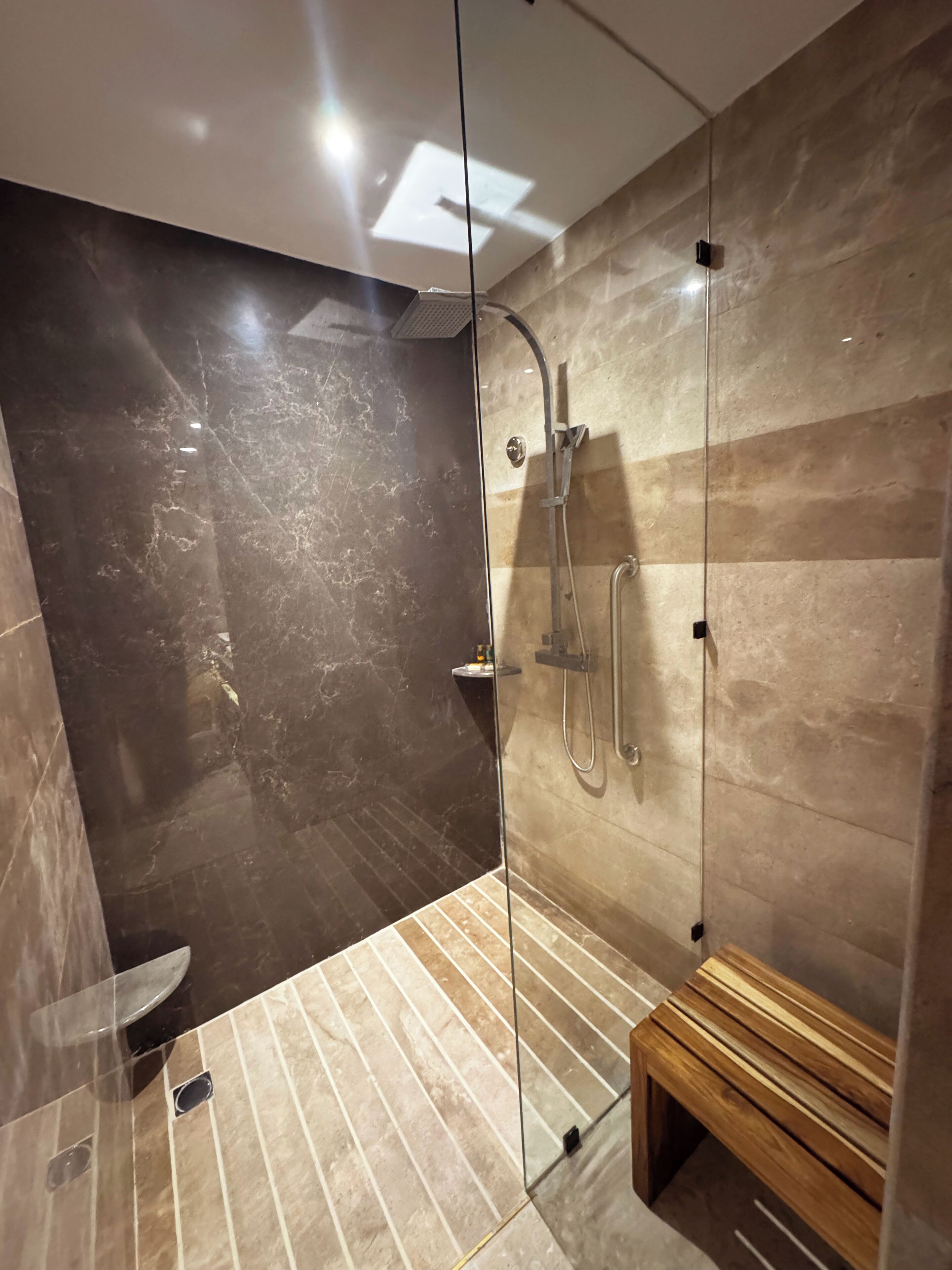 A modern bathroom with a glass-enclosed shower, a wooden bench, and a toilet.