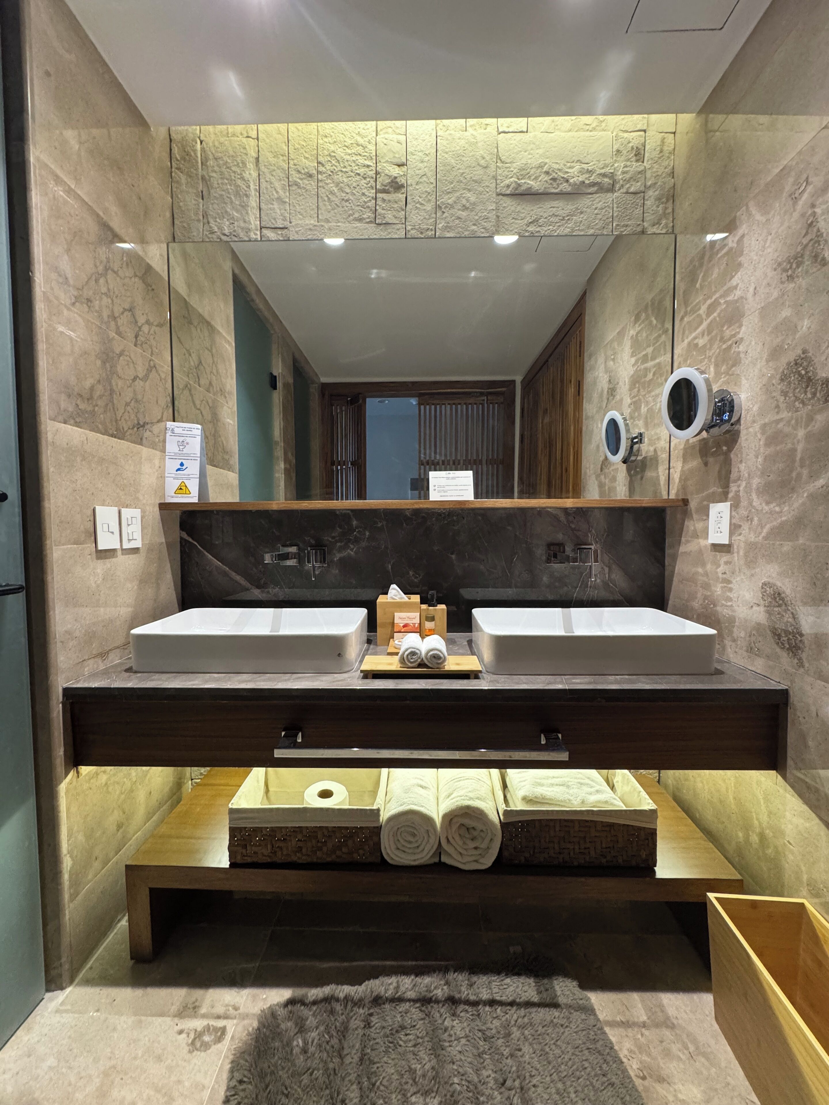 Ein modernes Badezimmer mit zwei Waschbecken, einem großen Spiegel und einer Holzausstattung mit Stauraum.