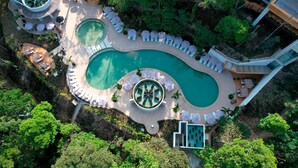 Vue aérienne d’un complexe hôtelier doté d’une grande piscine centrale, de plusieurs piscines plus petites et de chaises longues disposées autour des piscines.