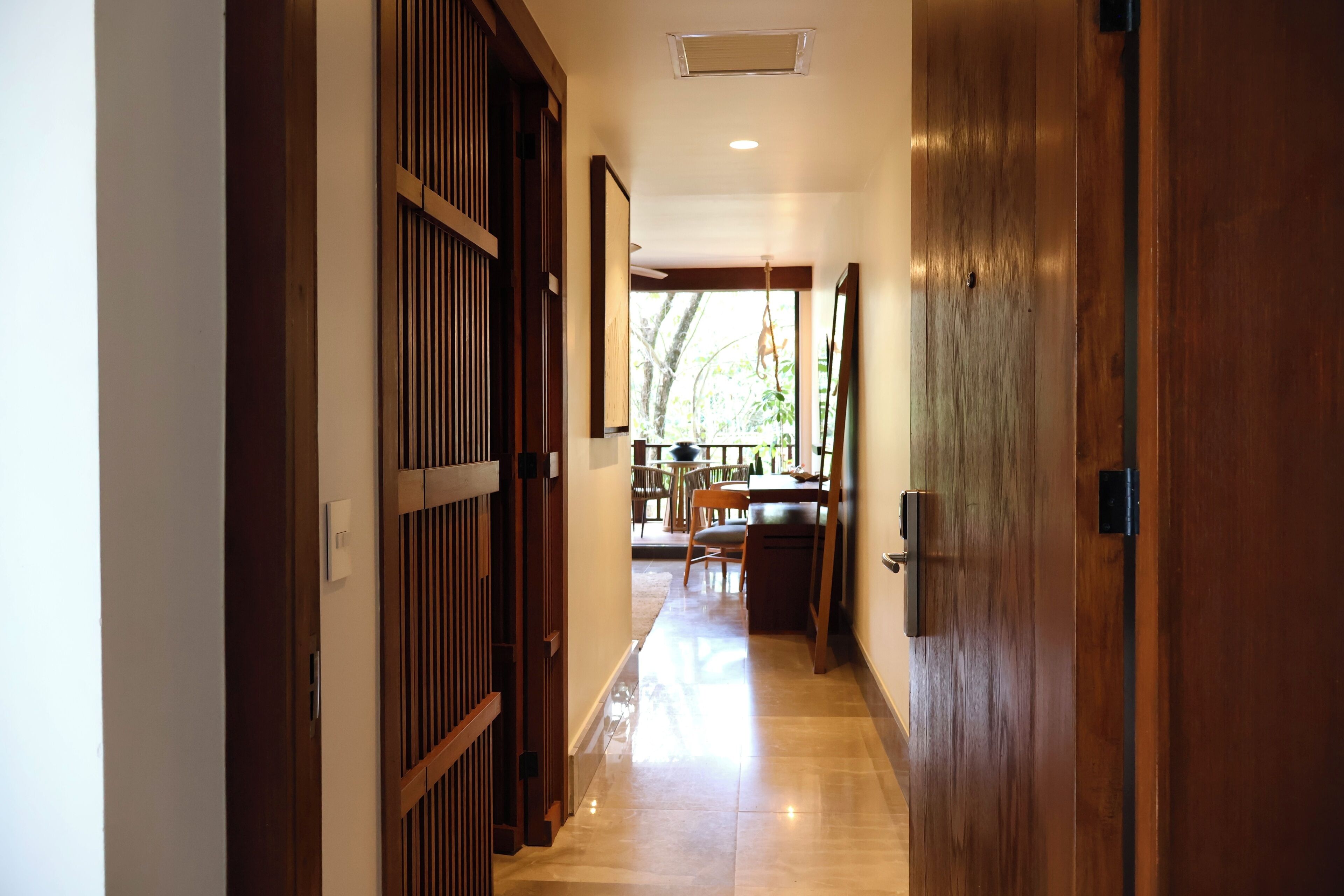 A hallway with wooden doors and a tiled floor leading to a dining area with tables and chairs.