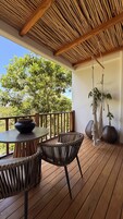A wooden deck with a round table and chairs, a hanging macrame plant, and a view of trees.
