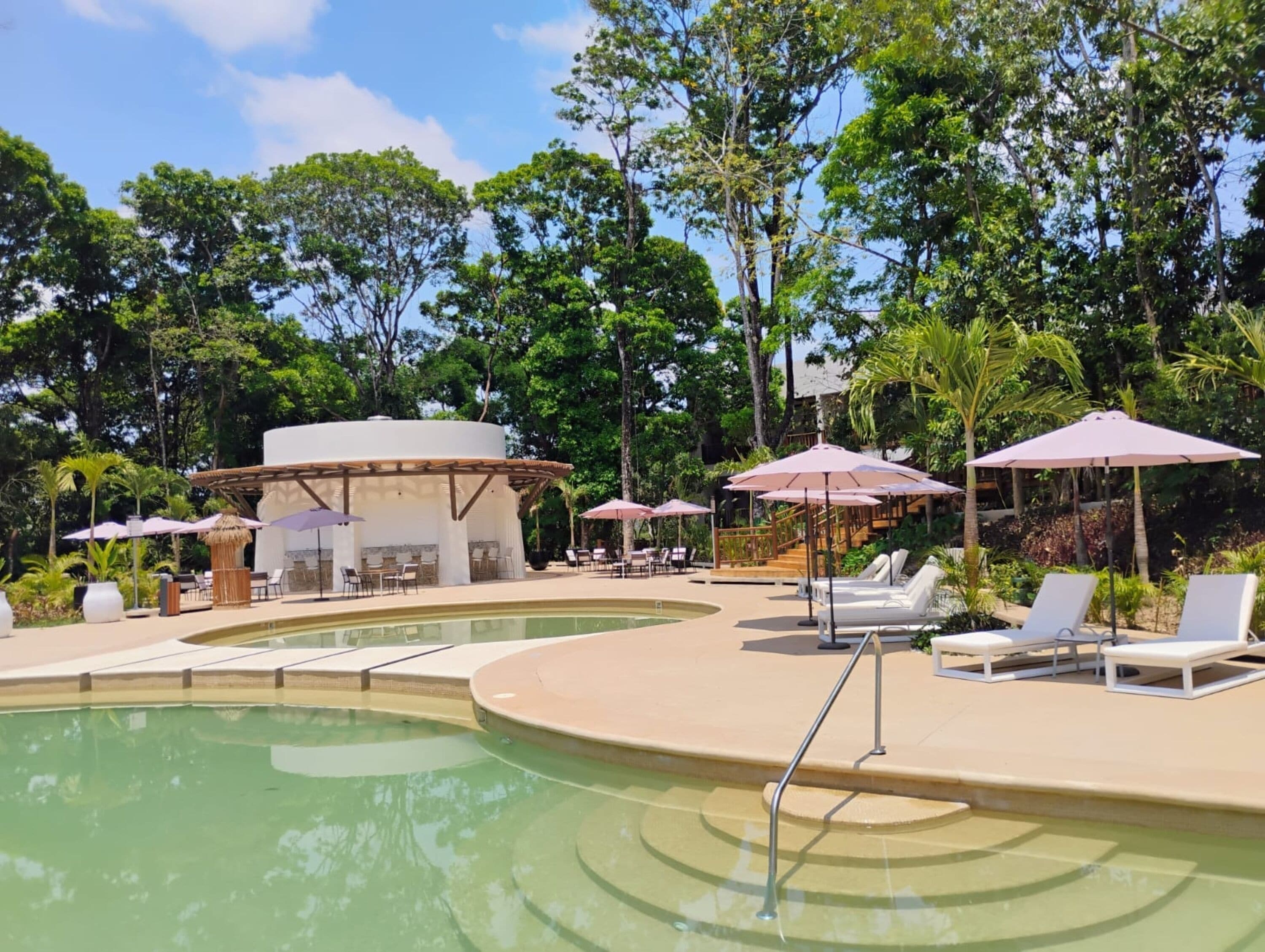 Un área de piscina con sillones de descanso, sombrillas y un pabellón.