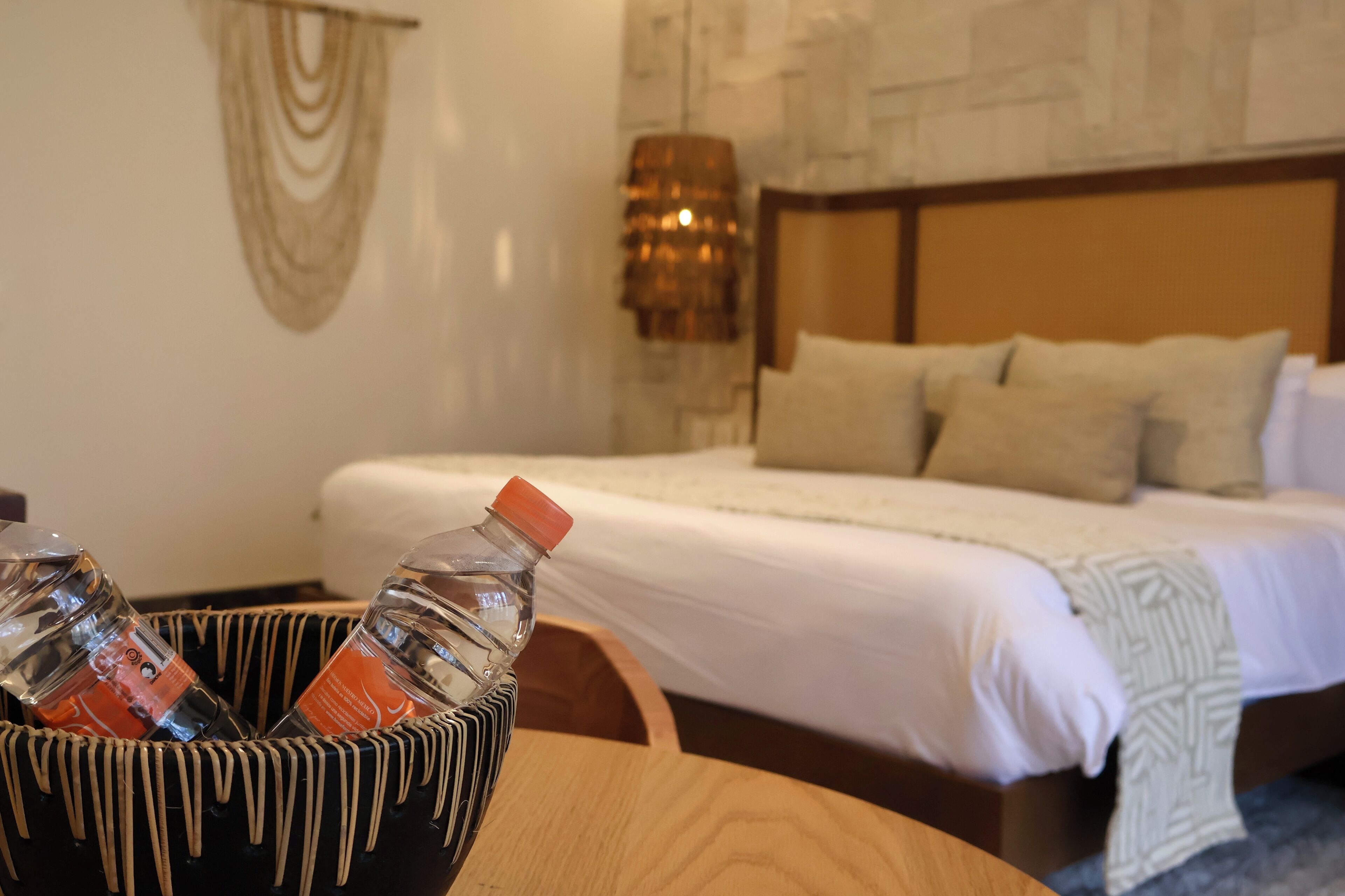 A hotel room with a bed, a bedside lamp, and a wooden table with a bottle of water.