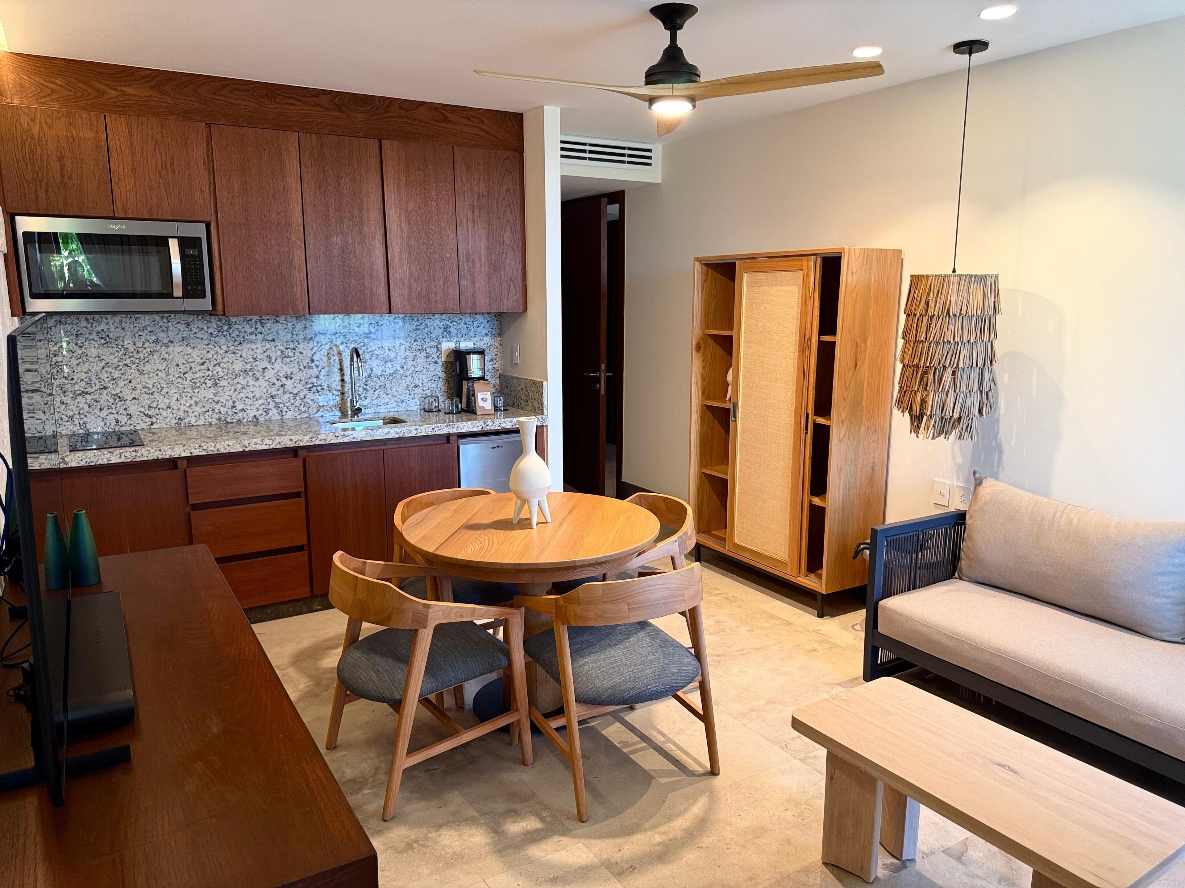 A modern kitchen with wooden cabinets, a microwave, and a granite countertop. There is a dining area with a wooden table and chairs, and a sofa in the living room.