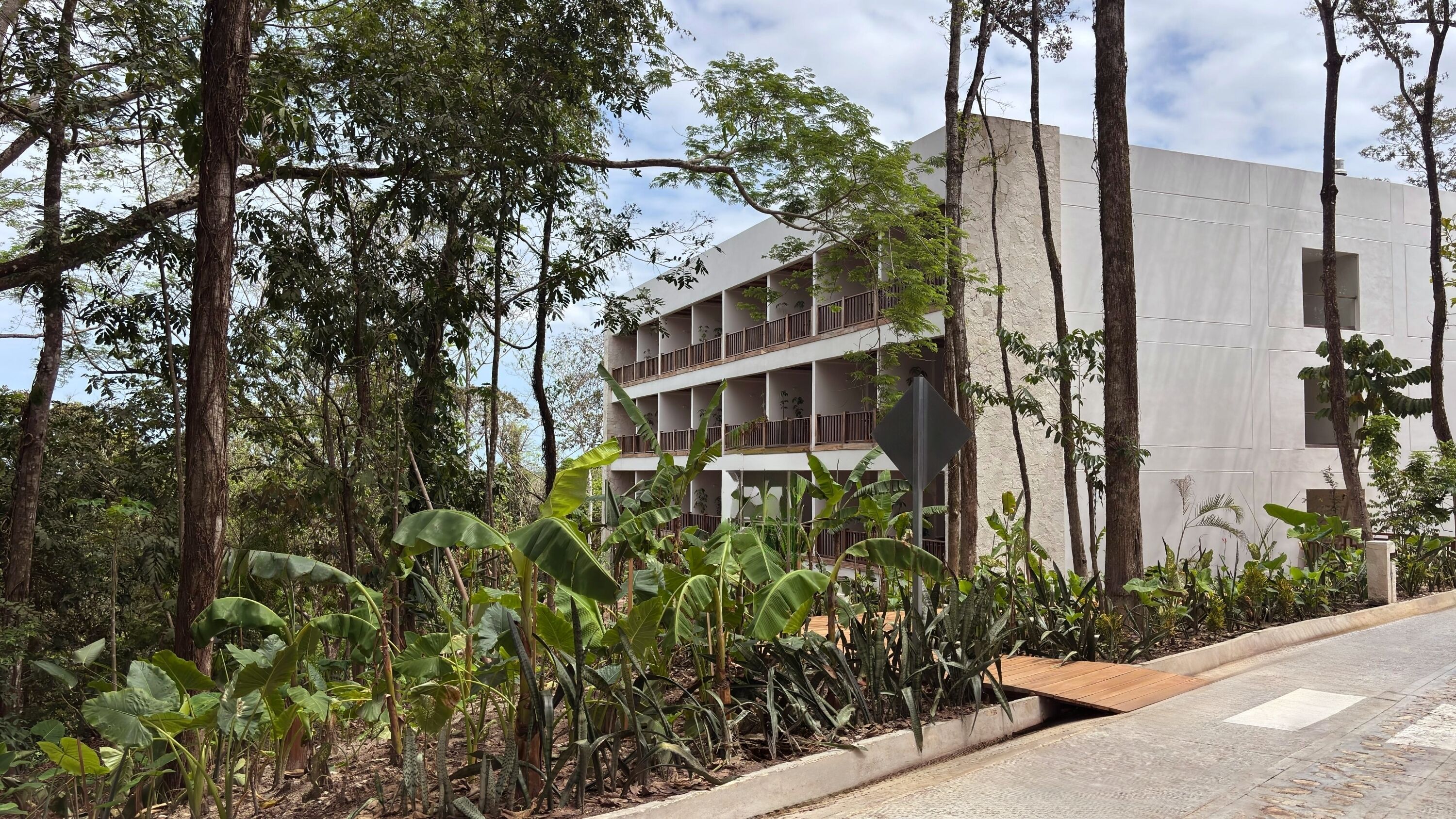 Un bâtiment moderne doté de nombreux balcons, entouré d’une végétation tropicale luxuriante.