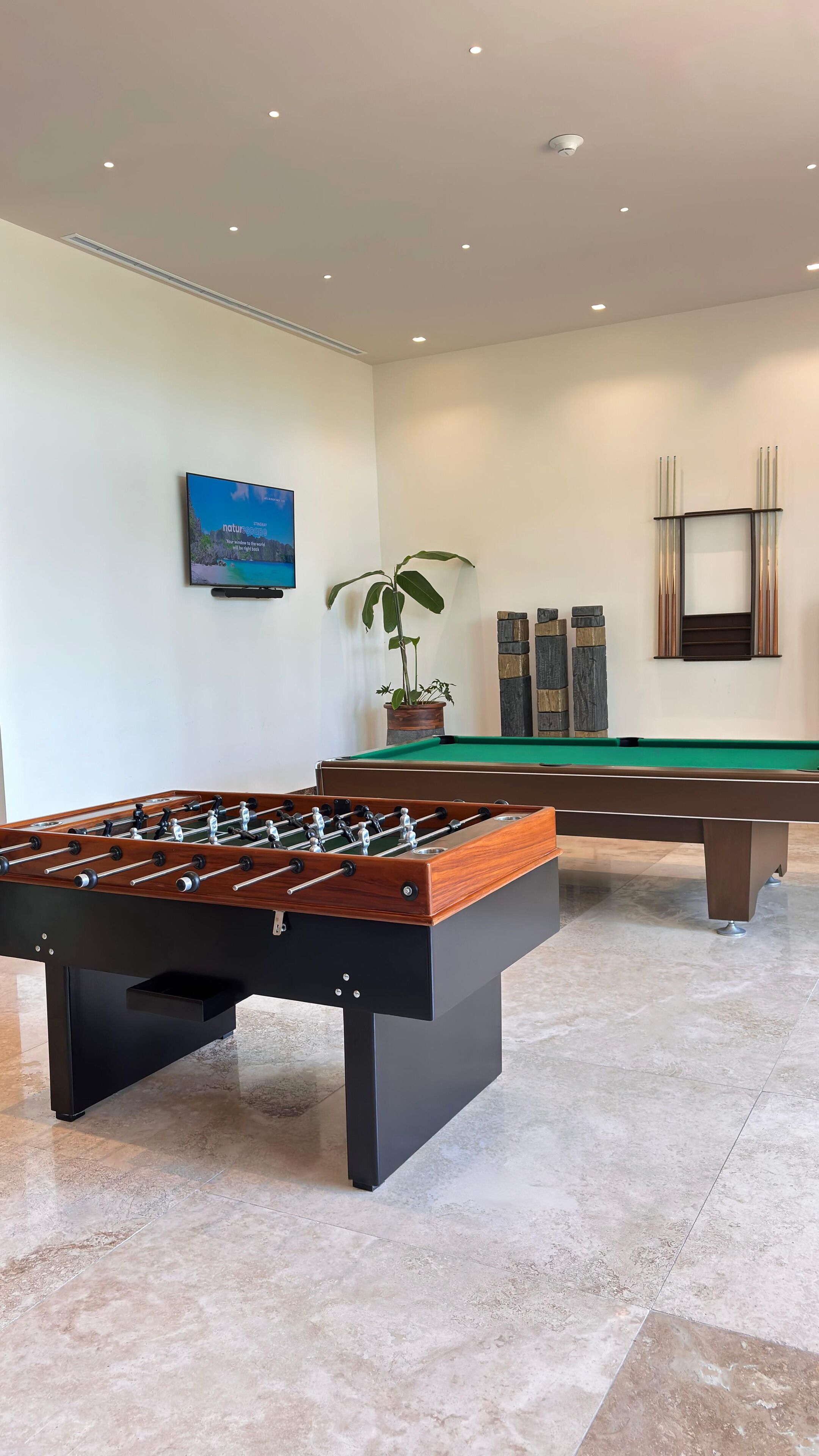 A room with a foosball table, a pool table, and a painting on the wall.