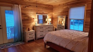 Een slaapkamer in een houten blokhut, met een bed, een ladekast en een spiegel.