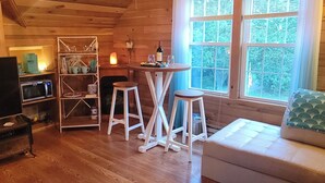 Een gezellig interieur van een chalet met houten vloeren, een bank, een eettafel met krukken, een televisie en een boekenkast.