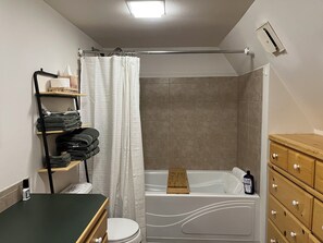 Et badeværelse med badekar, toilet og en trækommode med skuffer.