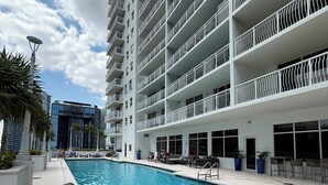 Um hotel moderno com piscina, várias varandas e vista para edifícios próximos.