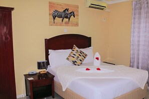 Een net opgemaakt bed met een witte deken en een decoratief kussen, een nachtkastje met een lamp, en wanddecoratie met een zebra thema.