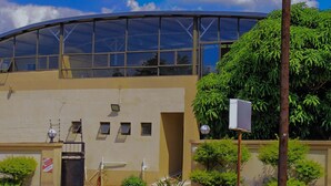A modern building with a curved glass roof, a beige facade, and a gated entrance. - Comfort Palace  (Kasane)