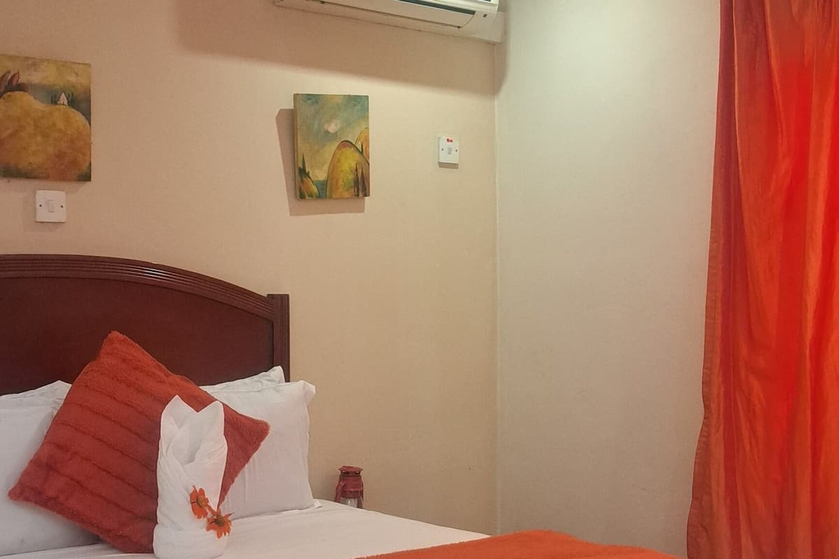 Una cama bien hecha con una colcha blanca y naranja, un cabecero de madera y dos cuadros colgados en la pared.