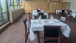 A restaurant with outdoor wooden flooring, tables set with white tablecloths, and chairs. - Comfort Palace  (Kasane)