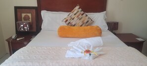Een netjes opgemaakt bed met witte lakens, een decoratieve handdoek met bloemen en een lijstfoto op het nachtkastje.