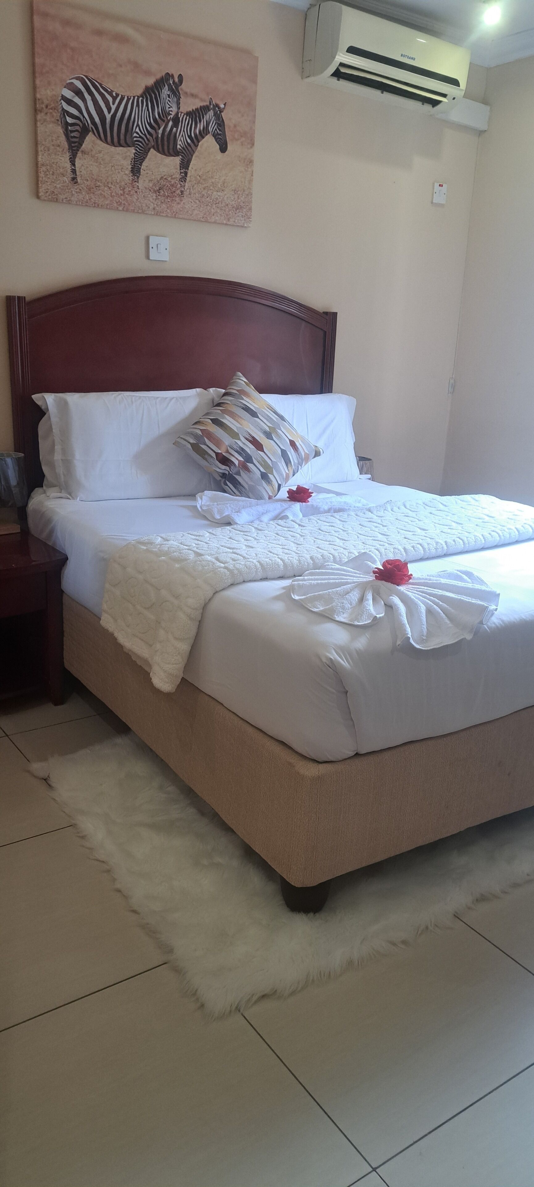 Una cama bien tendida con sábanas blancas, una alfombra mullida de color blanco y una obra de arte con temática de cebra sobre ella.