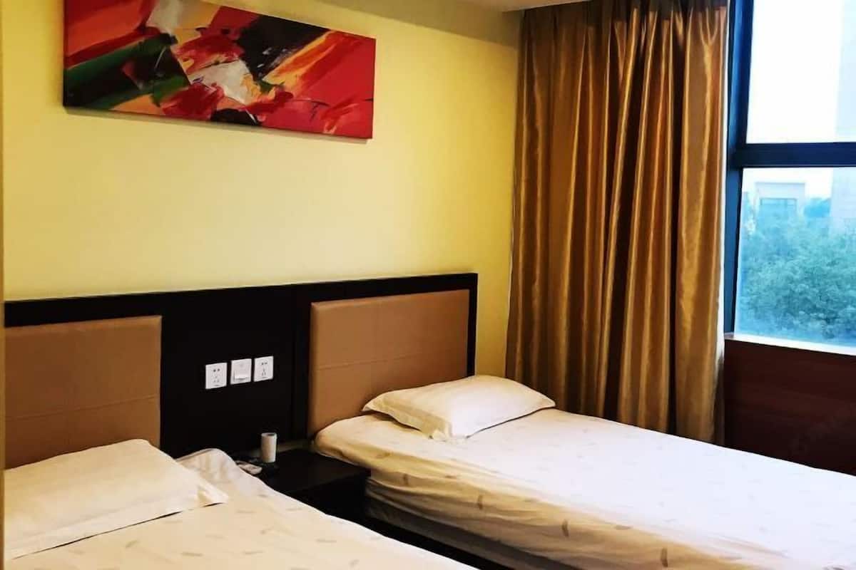 A hotel room with two beds, a headboard, a painting on the wall, and a window with curtains.