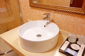 Un lavabo blanc dans la salle de bain, avec un seul robinet, un miroir au-dessus et un plateau contenant des articles de toilette.