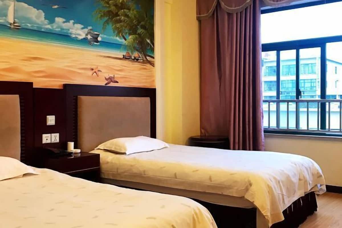 A hotel room with two beds, a beach-themed mural, a window with curtains, and a view of a building outside.