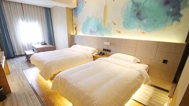 Habitación de hotel con dos camas, un escritorio, una silla, una mesita de noche y un cuadro abstracto grande en la pared.