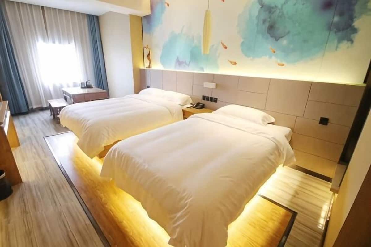 A hotel room with two beds, a desk, a chair, a nightstand, and a large abstract painting on the wall.