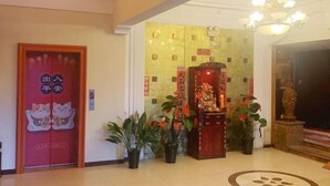 Vestíbulo de hotel con una puerta roja decorada con un felino, una araña y plantas en macetas.