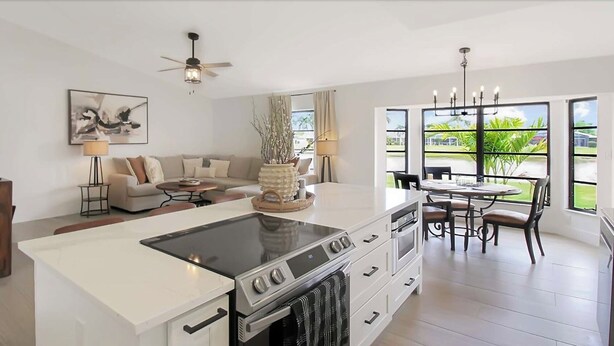 A modern kitchen with a central island, dining area with a table and chairs, a sofa set, and a large window with a view of greenery. - Welcome to Punta Paradise! Book Now! (Punta Gorda)