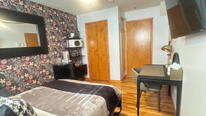 A bedroom with a bed, a desk, a chair, a ceiling fan, a mirror, and a wardrobe. - Amelia Suites Newark – Cozy stay with AC, Wi-Fi & NYC access! (Newark)