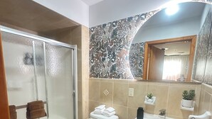 A bathroom with a glass-enclosed shower, a toilet, a sink, and a mirror. - Amelia Suites Newark – Cozy stay with AC, Wi-Fi & NYC access! (Newark)