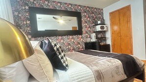 A bedroom with a bed, a ceiling fan, a TV, a wardrobe, and a shelf with items. - Amelia Suites Newark – Cozy stay with AC, Wi-Fi & NYC access! (Newark)